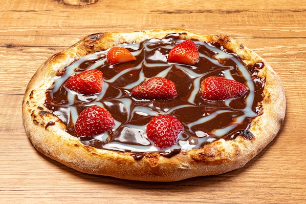 chocolate pizza with strawberry and sour cream sauce served on a wooden table