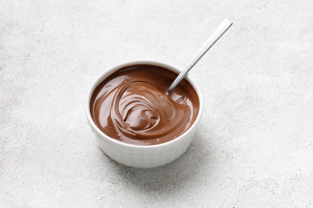 Chocolate sauce in a white saucer with spoon on grey background Curl of Liquid chocolate Copy space