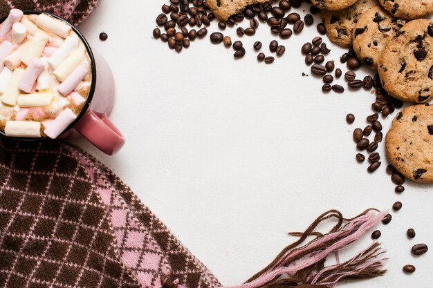 Chocolate scone and cup of latte with marshmallow, warm cozy scarf nearby, top view, free space in the middle. Delicious cold morning with cookies and hot drink