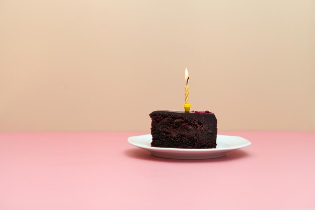 Chocolate slice cake with candle on pink backgroundhappy birthday tart minimalistic image