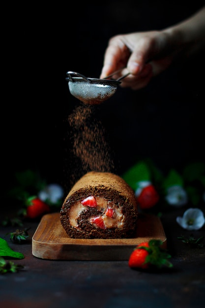 Chocolate strawberry sweet roll with levitating strawberries and woman hands,dark food photography