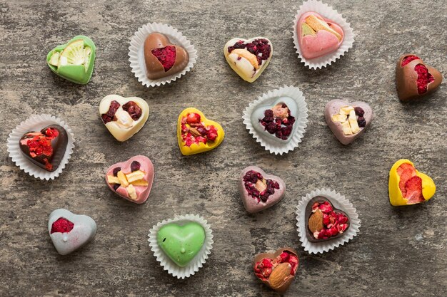 chocolate sweets in the form of a heart with fruits and nuts on a colored background top view with space for text holiday concept