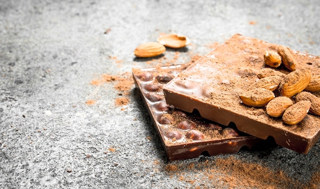 Chocolate with nuts and cocoa powder on rustic table.