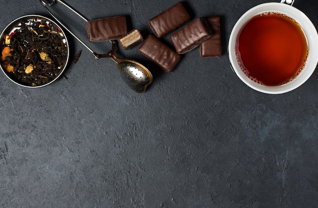 Chocolates and black tea with herbs. Metal tea strainer. 