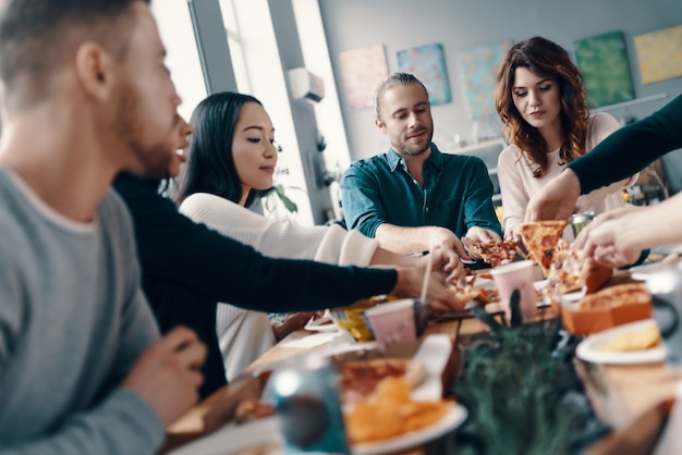 Choosing the best slice. Group of young people in casual wear picking pizza and smiling while having a dinner party indoors