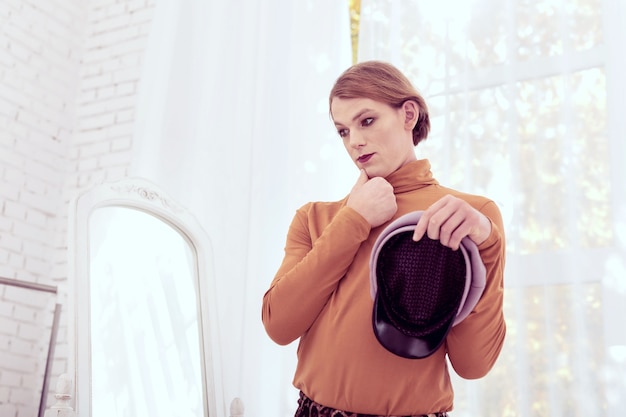 Photo choosing better variants. thoughtful transgender man thinking about hat choices while carrying newsboy cap