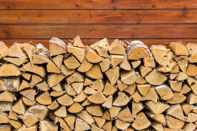 Chopped birch firewood on brown wooden wall background