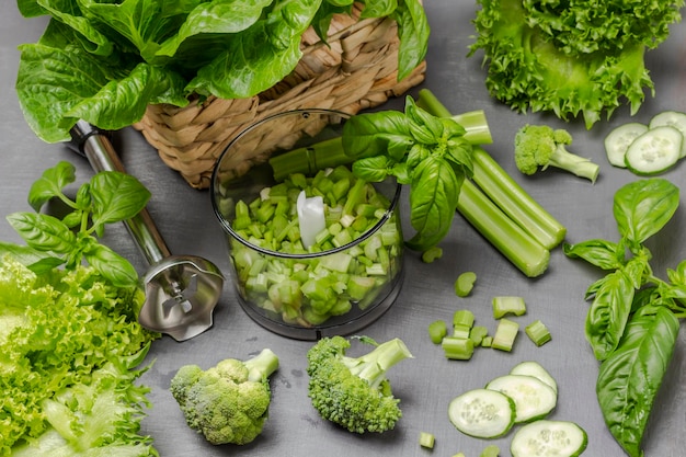 Chopped celery stalks in blender Broccoli cucumbers lettuce on table