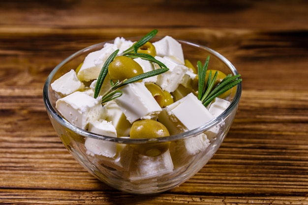 Chopped feta cheese rosemary and olives in glass bowl on a wooden table