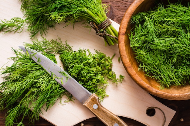 Chopped fresh dill on a cutting board and dill in a wood bowl on the table. Top view