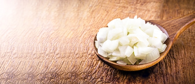 Chopped onion and garlic in wooden spoon used in rustic kitchen setting, seasoning ingredient.