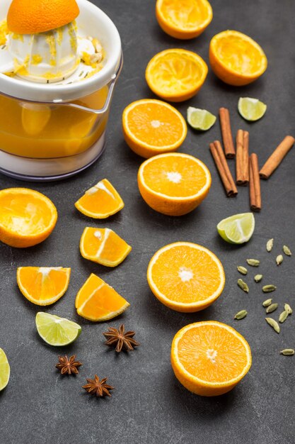 Chopped oranges and cinnamon sticks on table. Juicer with orange peel. Black background. Top view