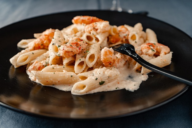 A chopped view of a black plate served with dry penne rigate pasta with an exquisite shrimp and prawn cream.