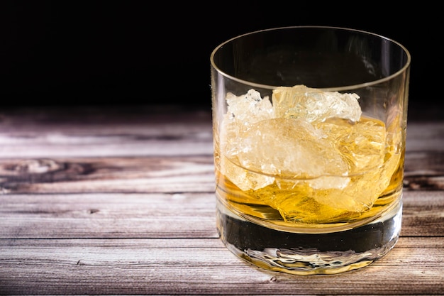 Chopped view of a glass with whiskey or scotch and large chunks of ice on a rustic wooden table