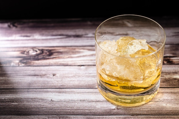 Chopped view of a glass with whiskey or scotch and large chunks of ice on a rustic wooden table