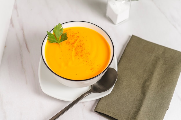 Chopped view of a white bowl with cream of squash and carrots soup with a green napkin