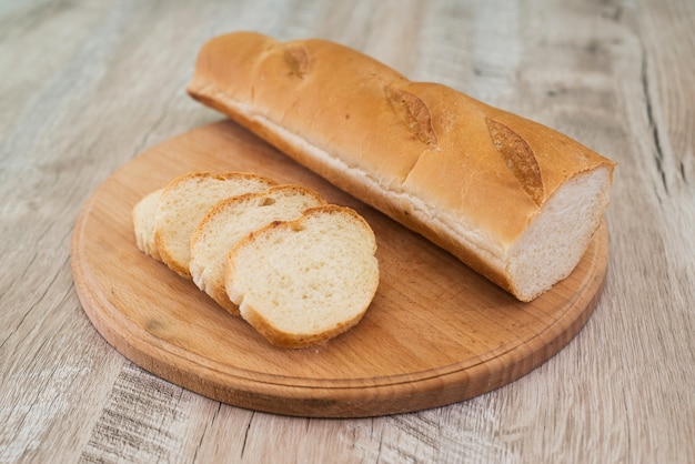 A chopped whole grain baguette lies on a wooden board. Delicious sliced French baguette on a wooden table.