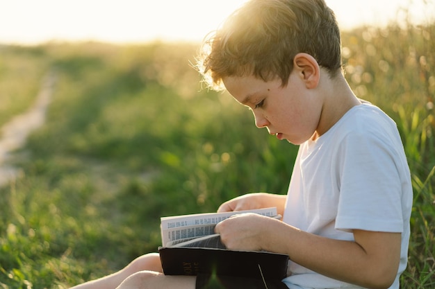 Christian boy holds bible in her hands Reading the Holy Bible in a field during beautiful sunset Concept for faith spirituality and religion Peace hope