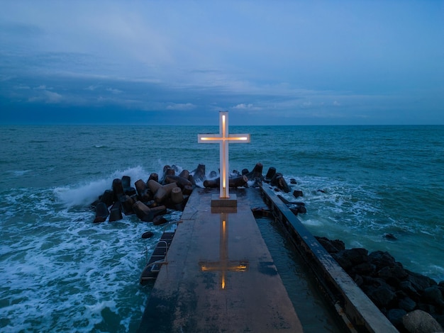 Christian cross standing on pier in the sea or ocean with dramatic sky at night