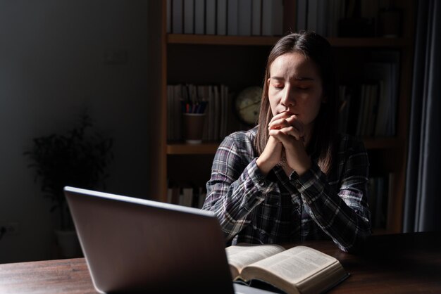 Christian online technology concept Hands praying of christian with digital computer laptop Online live church for sunday service Asian catholic man are reading Holy bible book and online study