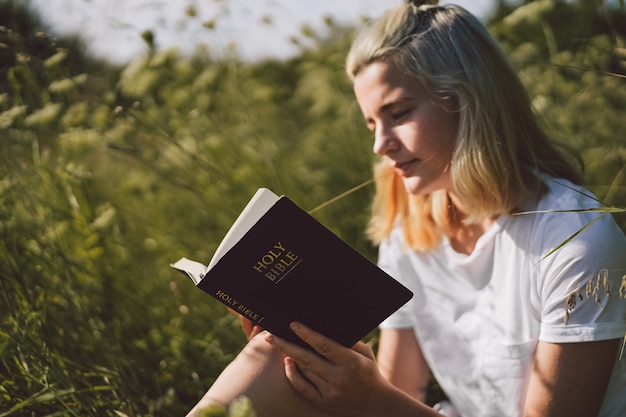 Christian teenage girl reading the Bible in the field. Faith, spirituality and religion concept. 