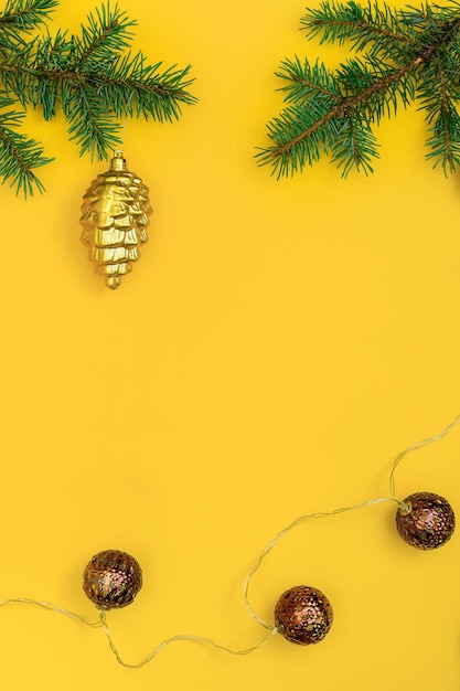 Christmas background: fir-tree branches, a toy pine cone and a garland with brown balls on a yellow background. Copy Space Center