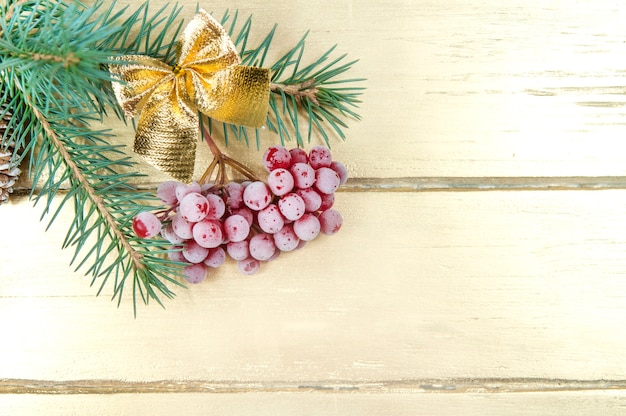 Christmas background, green spruce branch with a bunch of red berries and a gold bow on a gold table