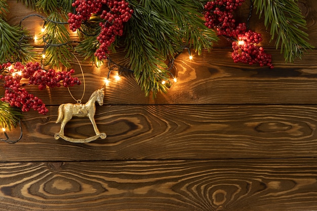 Christmas background. Nobilis fir branches, twigs with red berries, toy golden horse on brown wooden planks. Copy space, flat lay, top view. Holiday, Xmas, New Year concept. Mockup.