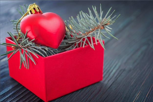 Christmas background: red gift box with a Christmas toy in the form of a heart and fir branches