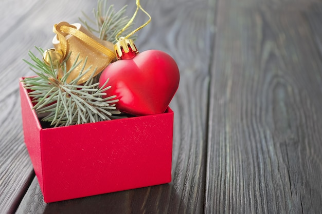 Christmas background: red gift box with a Christmas toy in the form of a heart, a golden bell and fir branches,