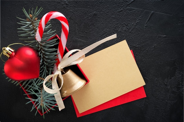 Christmas background: red gift box with a Christmas toy in the shape of a heart, a golden bell , fir branches and card for congratulatory text