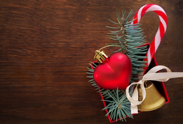 Christmas background: red gift box with a Christmas toy in the shape of a heart, a golden bell , fir branches and christmas candy 