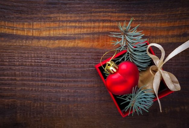 Christmas background: red gift box with a Christmas toy in the shape of a heart, a golden bell and fir branches