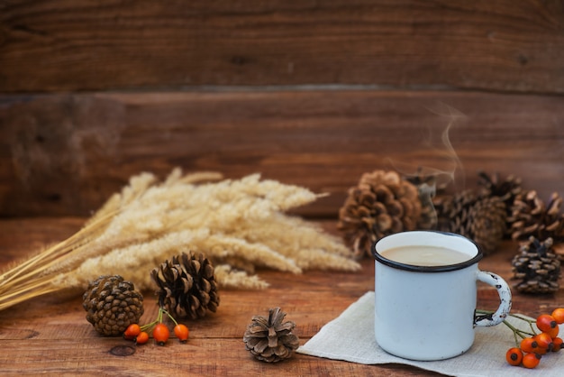 Christmas background in rustic style. A metal mug with hot milk tea stands on a tablecloth, on a wooden surface among pine cones, spruce branches, spikelets of wheat and rosehips. Copy Space, Flat lay