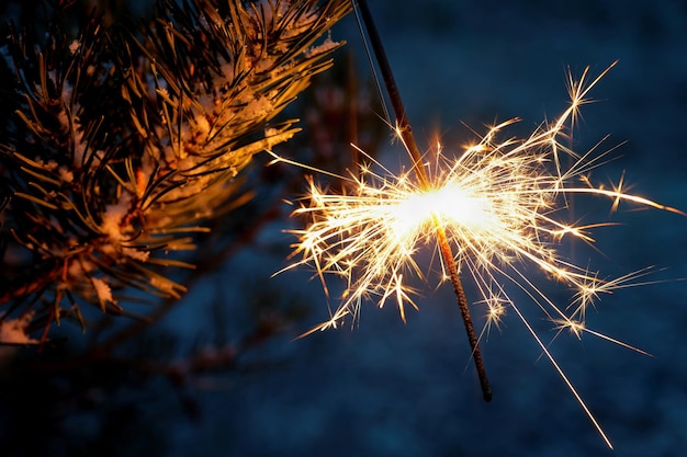 Christmas background A sparkler on a Christmas tree in the evening outside with snow Concept for winter season holidays and new year 2023