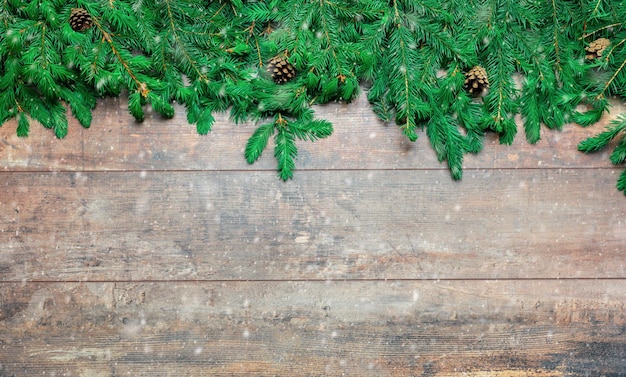 Christmas Background template Frame made of fir tree branches with snowflakes and ice crystals on brown wooden texture top view with space for text