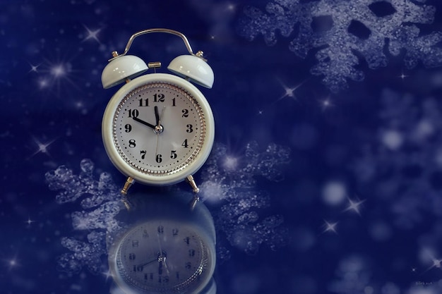 Christmas background white alarm clock on a blue background falling snowflakes space for text