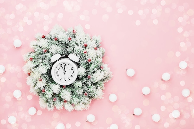 Christmas background. White Christmas wreath and alarm clock on pink background. Copy space, top view