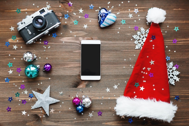 Christmas background with smartphone, old fashioned camera, red Santa's hat, decorations