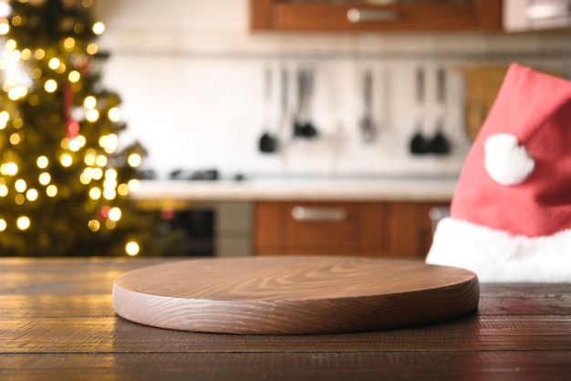 Christmas background with wooden table top, Santa hat, and blurred kitchen.