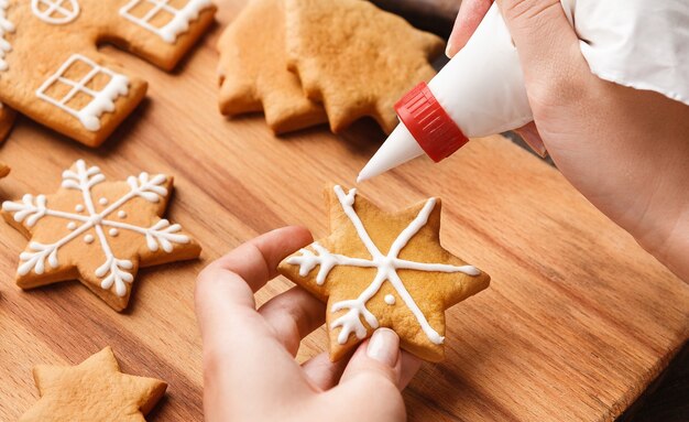 Photo christmas bakery. woman decorating homemade gingerbread snowflake cookie with icing, closeup