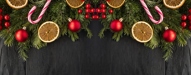 Christmas banner with spruce branches dried orange and red bead on the black wooden background Copy space