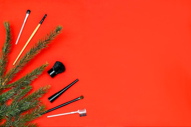 Christmas beauty cosmetics composition with brushes tools and accessories with new year fir spruce branches decorations on red background Stylish concept Flat lay mock up top view with copy space