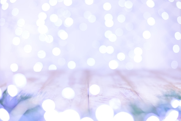 Christmas bokeh background with fir branches and an empty light wooden table.