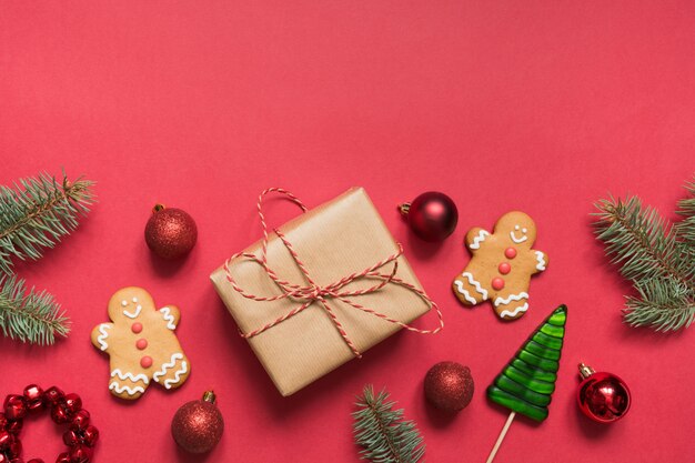 Christmas border of gift box, evergreen branches, gingerbread cookies on red. Xmas holiday. 