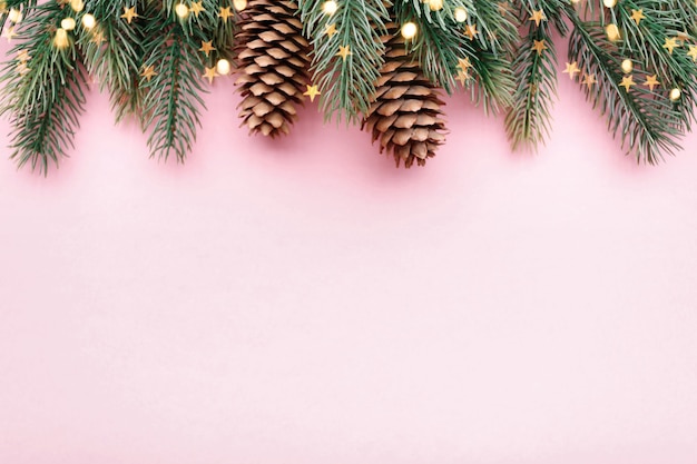 Christmas border with fir branches and conifer cones on pastel pink background, copy space