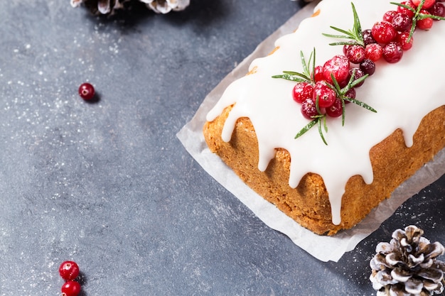 Christmas cake with sugar icing, cranberries and rosemary on a dark table. Copy space