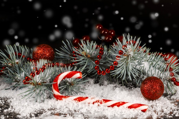 Christmas candy cane and red christmas balls with fir branch on black background with snow.