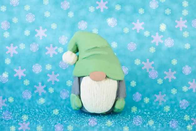 Christmas card figurine of a funny gnome with a beard and a big nose on a blue background and falling snowflakes.