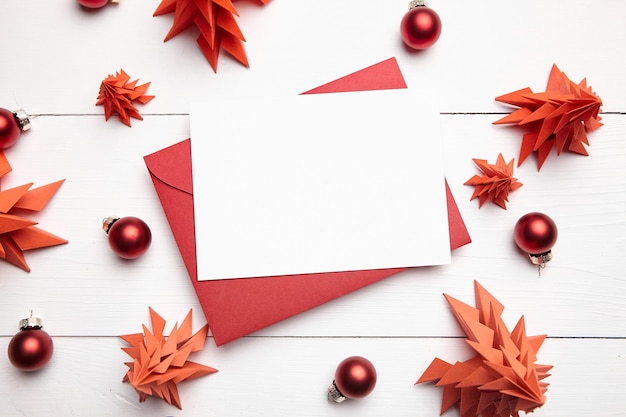 Christmas card mockup with envelope and red paper fir trees on white wooden background top view flat lay